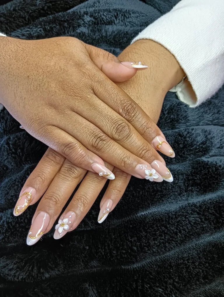 Detalle artístico de manicura con flores blancas tridimensionales y finos hilos de oro en el salón Eli